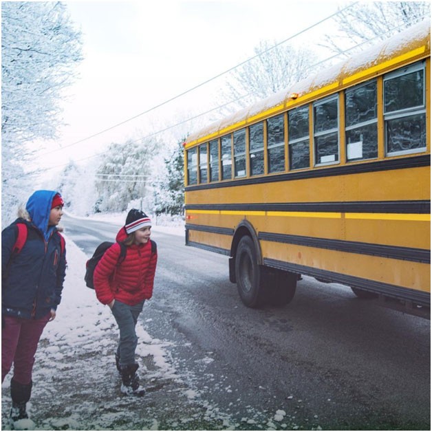 A couple of kids walking on a road next to a school busDescription automatically generated